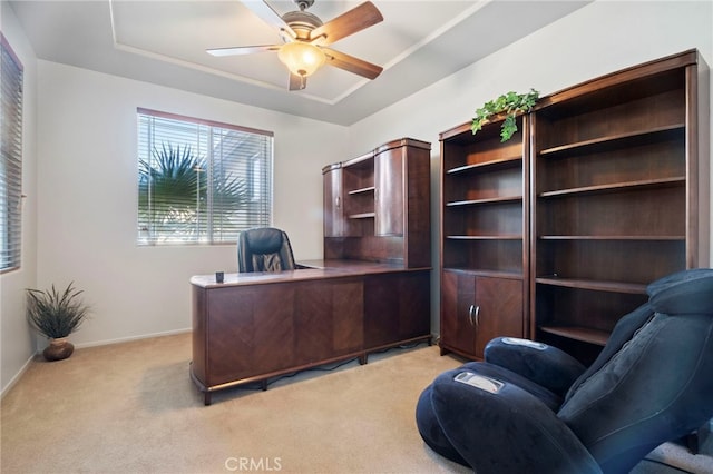 office space with a tray ceiling, light colored carpet, baseboards, and ceiling fan