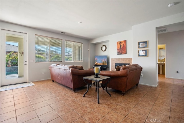 living room with light tile patterned floors, visible vents, a tile fireplace, and baseboards