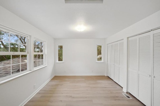 unfurnished bedroom with multiple closets and light hardwood / wood-style floors