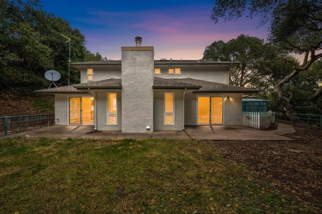 back house at dusk featuring a lawn and a patio