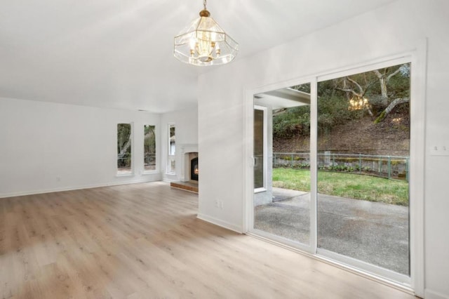 unfurnished living room featuring plenty of natural light, an inviting chandelier, and light hardwood / wood-style floors