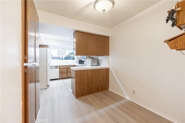 kitchen with a textured ceiling, kitchen peninsula, white appliances, and light wood-type flooring