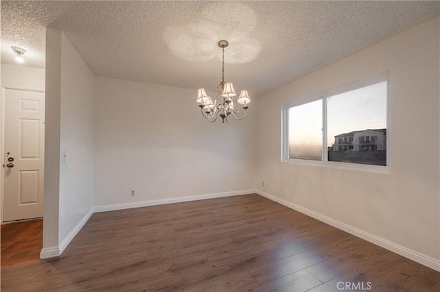 spare room with dark hardwood / wood-style flooring, a textured ceiling, and an inviting chandelier