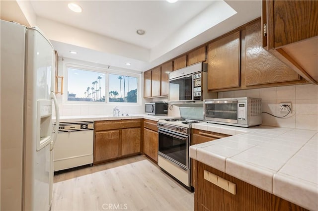 kitchen featuring sink, tile counters, tasteful backsplash, white appliances, and light wood-type flooring