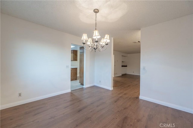 unfurnished dining area featuring a notable chandelier, dark hardwood / wood-style flooring, and a textured ceiling