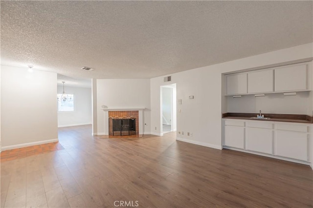 unfurnished living room with a tiled fireplace, sink, a textured ceiling, wood-type flooring, and a chandelier