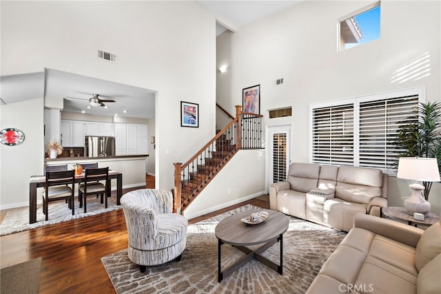 living area featuring visible vents, dark wood-style floors, stairway, baseboards, and ceiling fan