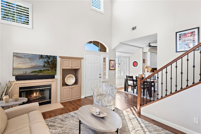 living area with visible vents, baseboards, ceiling fan, wood finished floors, and a glass covered fireplace