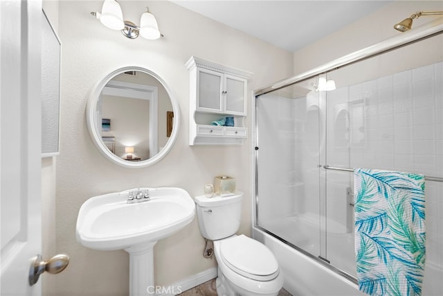 bathroom with toilet, baseboards, and shower / bath combination with glass door