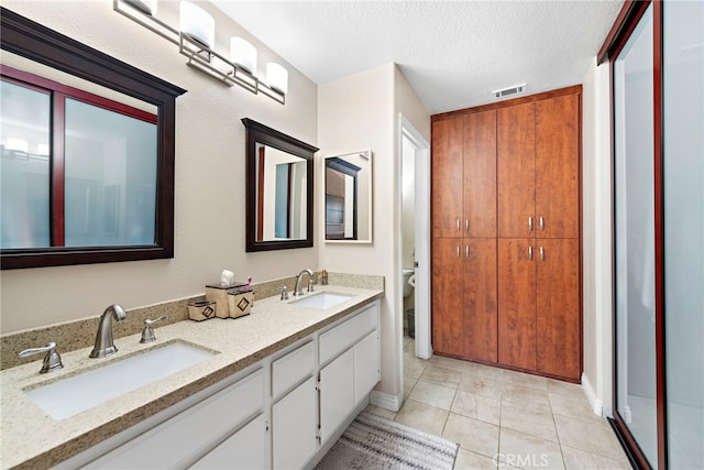 bathroom with toilet, a textured ceiling, walk in shower, tile patterned flooring, and vanity