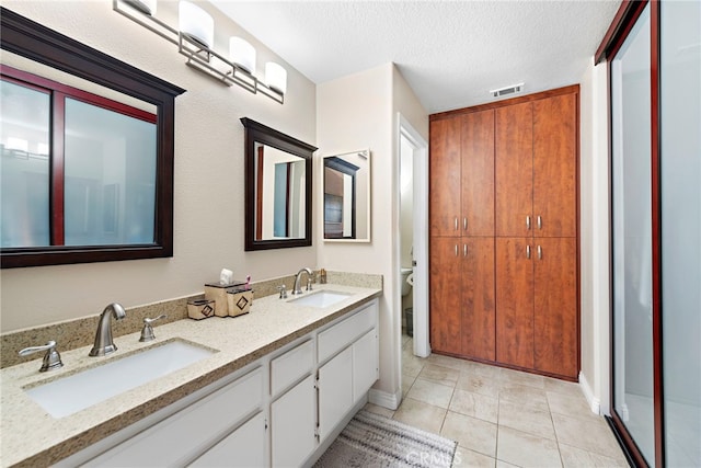 bathroom with a textured ceiling, tile patterned floors, visible vents, and a sink