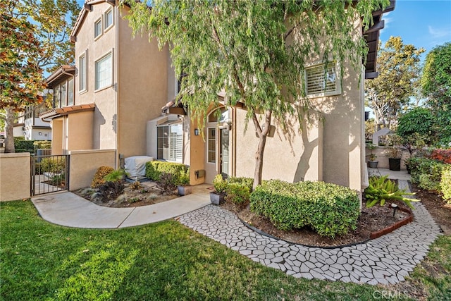 view of property exterior with a gate, a lawn, fence, and stucco siding