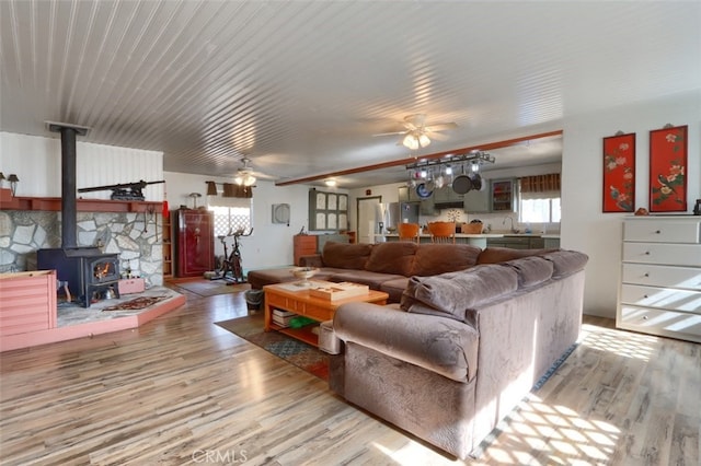 living room featuring ceiling fan, a wood stove, and light hardwood / wood-style flooring