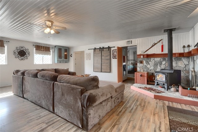 living room featuring ceiling fan, a wood stove, and light hardwood / wood-style flooring