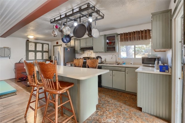 kitchen with a kitchen breakfast bar, sink, light wood-type flooring, kitchen peninsula, and stainless steel appliances