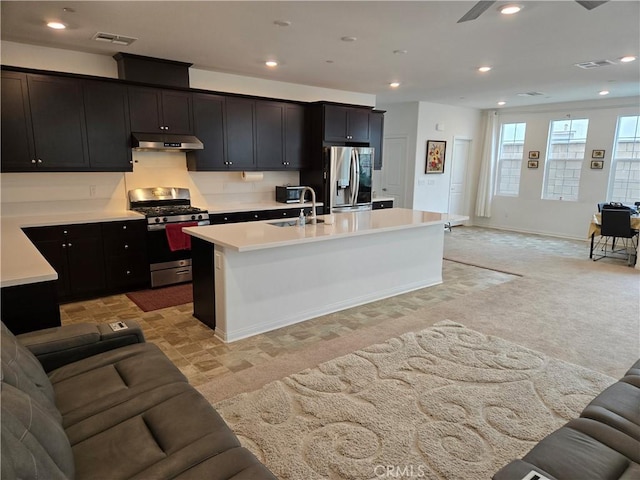 kitchen featuring light carpet, sink, stainless steel appliances, and an island with sink