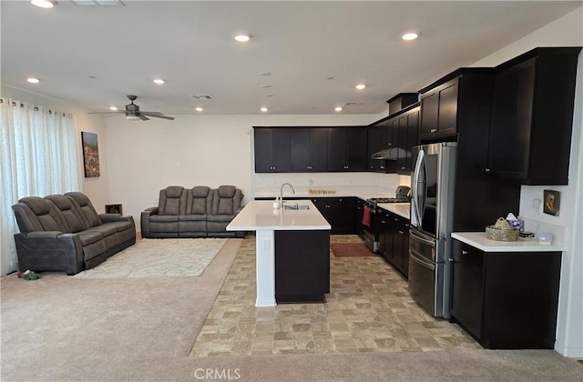 kitchen with ceiling fan, sink, an island with sink, light colored carpet, and appliances with stainless steel finishes