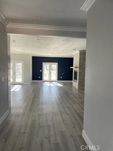 unfurnished living room with french doors, a stone fireplace, crown molding, and hardwood / wood-style floors