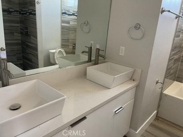 full bathroom featuring hardwood / wood-style floors, vanity, tiled shower / bath combo, and toilet