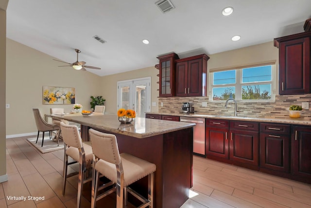 kitchen featuring sink, tasteful backsplash, stainless steel dishwasher, a kitchen bar, and a kitchen island