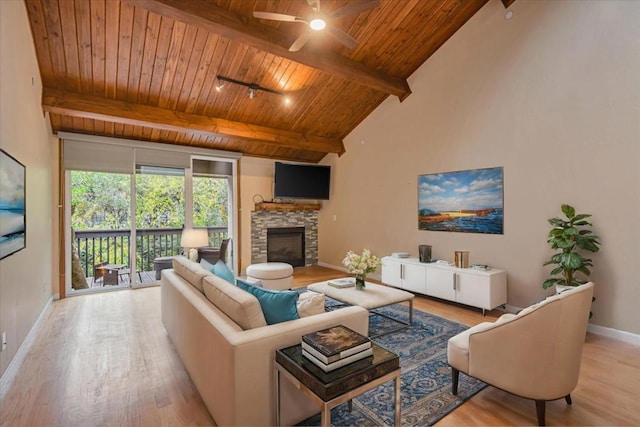 living room featuring ceiling fan, beamed ceiling, light wood-type flooring, a stone fireplace, and wooden ceiling