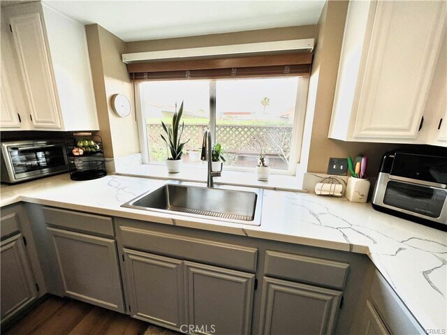 kitchen with light stone countertops, dark wood-type flooring, gray cabinetry, and sink