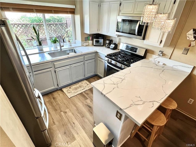 kitchen featuring kitchen peninsula, light wood-type flooring, a breakfast bar, stainless steel appliances, and sink