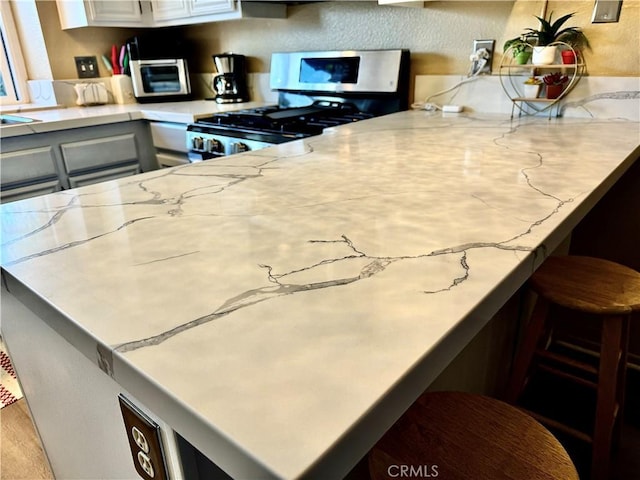 kitchen with kitchen peninsula, white cabinets, and stainless steel range with gas stovetop