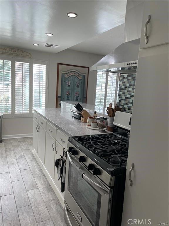 kitchen with extractor fan, light hardwood / wood-style flooring, white cabinetry, and stainless steel range with gas cooktop