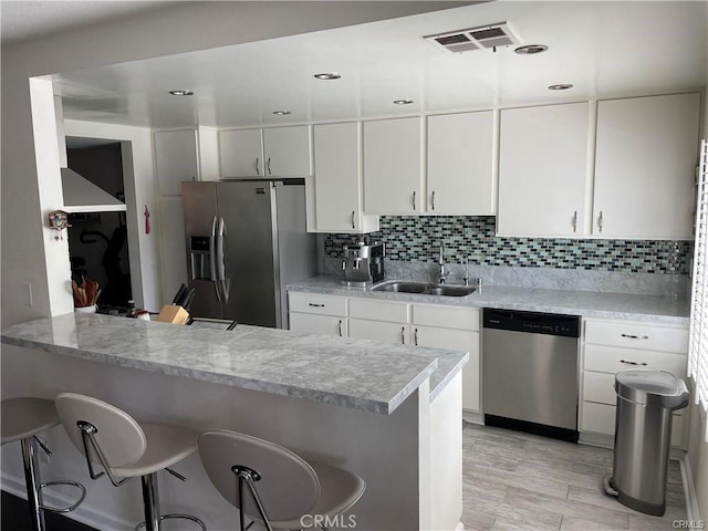 kitchen with sink, kitchen peninsula, appliances with stainless steel finishes, white cabinetry, and a breakfast bar area