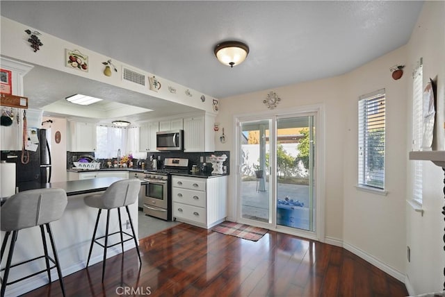 kitchen featuring dark hardwood / wood-style floors, a kitchen bar, white cabinetry, and stainless steel appliances