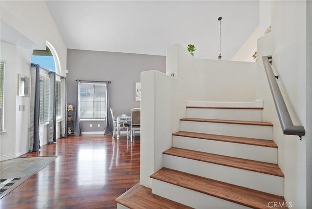 stairway with wood-type flooring and high vaulted ceiling