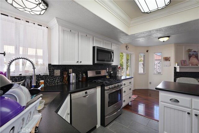 kitchen featuring backsplash, dark wood-type flooring, crown molding, white cabinetry, and stainless steel appliances