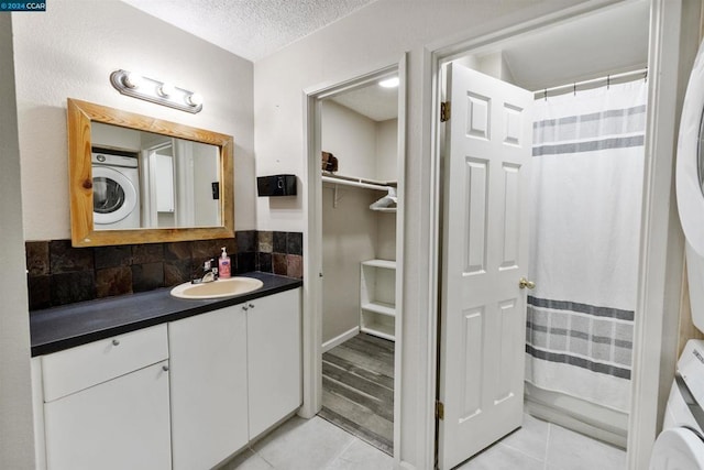 bathroom featuring vanity, tile patterned flooring, a textured ceiling, tasteful backsplash, and stacked washer / drying machine