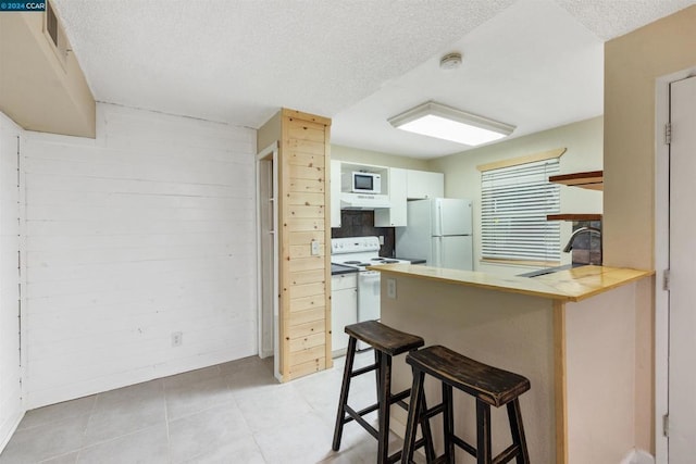 kitchen with white appliances, a kitchen breakfast bar, sink, a textured ceiling, and kitchen peninsula