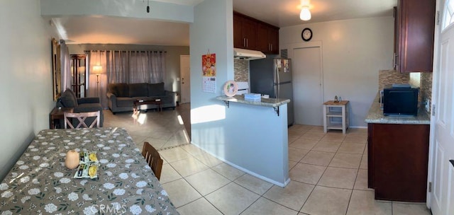 kitchen featuring under cabinet range hood, light tile patterned floors, freestanding refrigerator, and decorative backsplash