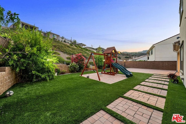 yard at dusk featuring a playground and a patio