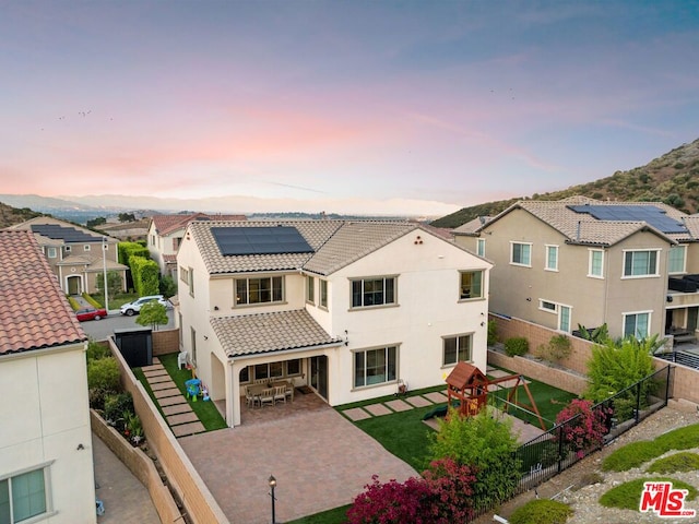 back house at dusk with a playground, a patio, and solar panels