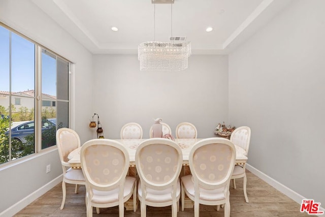 dining area with plenty of natural light, a raised ceiling, light wood-type flooring, and an inviting chandelier