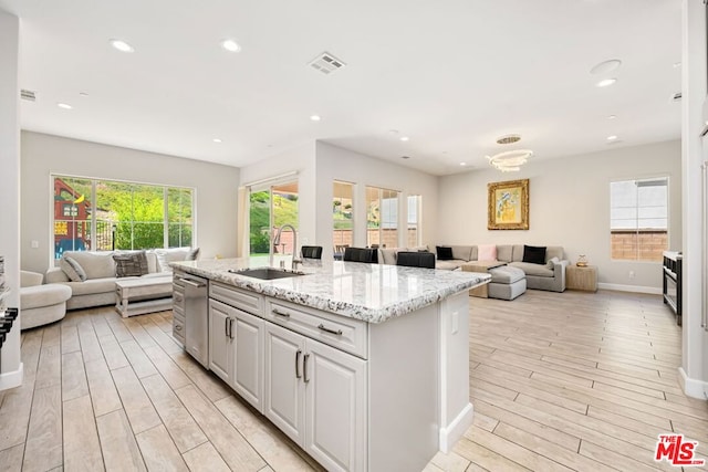 kitchen featuring light stone counters, sink, a center island with sink, light hardwood / wood-style floors, and white cabinetry