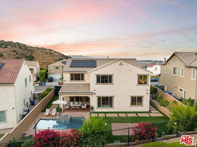 back house at dusk with solar panels, an outdoor hangout area, a fenced in pool, and a patio area