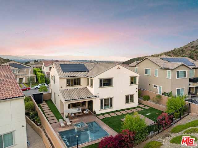 back house at dusk with a lawn, outdoor lounge area, solar panels, a fenced in pool, and a patio area