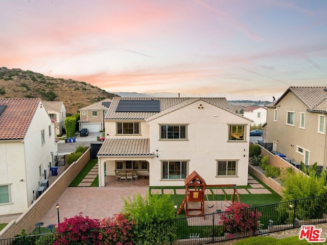 back house at dusk with a playground and solar panels