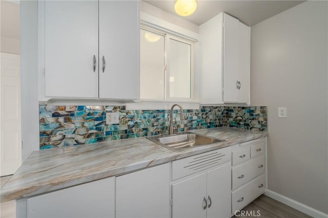 kitchen featuring decorative backsplash, light stone countertops, sink, hardwood / wood-style floors, and white cabinetry