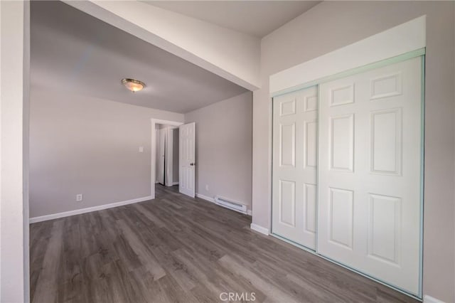 unfurnished bedroom featuring a baseboard heating unit, dark wood-type flooring, and a closet