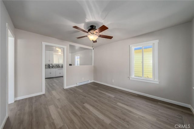 unfurnished room with hardwood / wood-style flooring, ceiling fan, and a baseboard heating unit