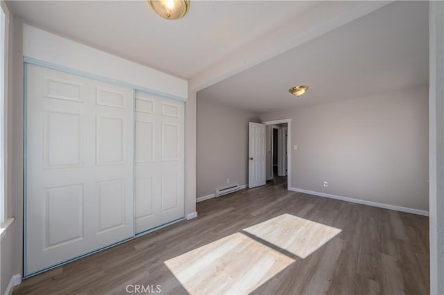 unfurnished bedroom featuring hardwood / wood-style flooring, a closet, and a baseboard heating unit