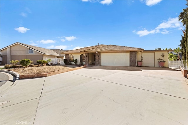 single story home featuring an attached garage, fence, a tile roof, concrete driveway, and stone siding