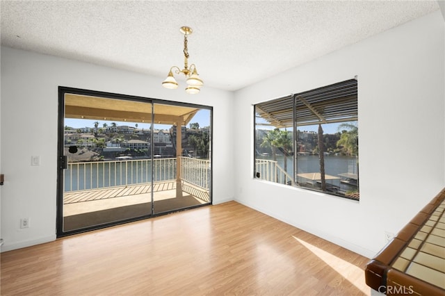 unfurnished dining area with a chandelier, a water view, a textured ceiling, and wood finished floors