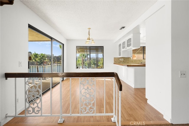 unfurnished dining area featuring baseboards, a textured ceiling, visible vents, and wood finished floors